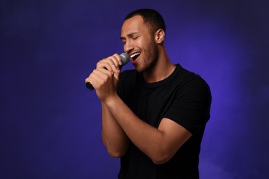 Photo of Handsome man with microphone singing on blue background