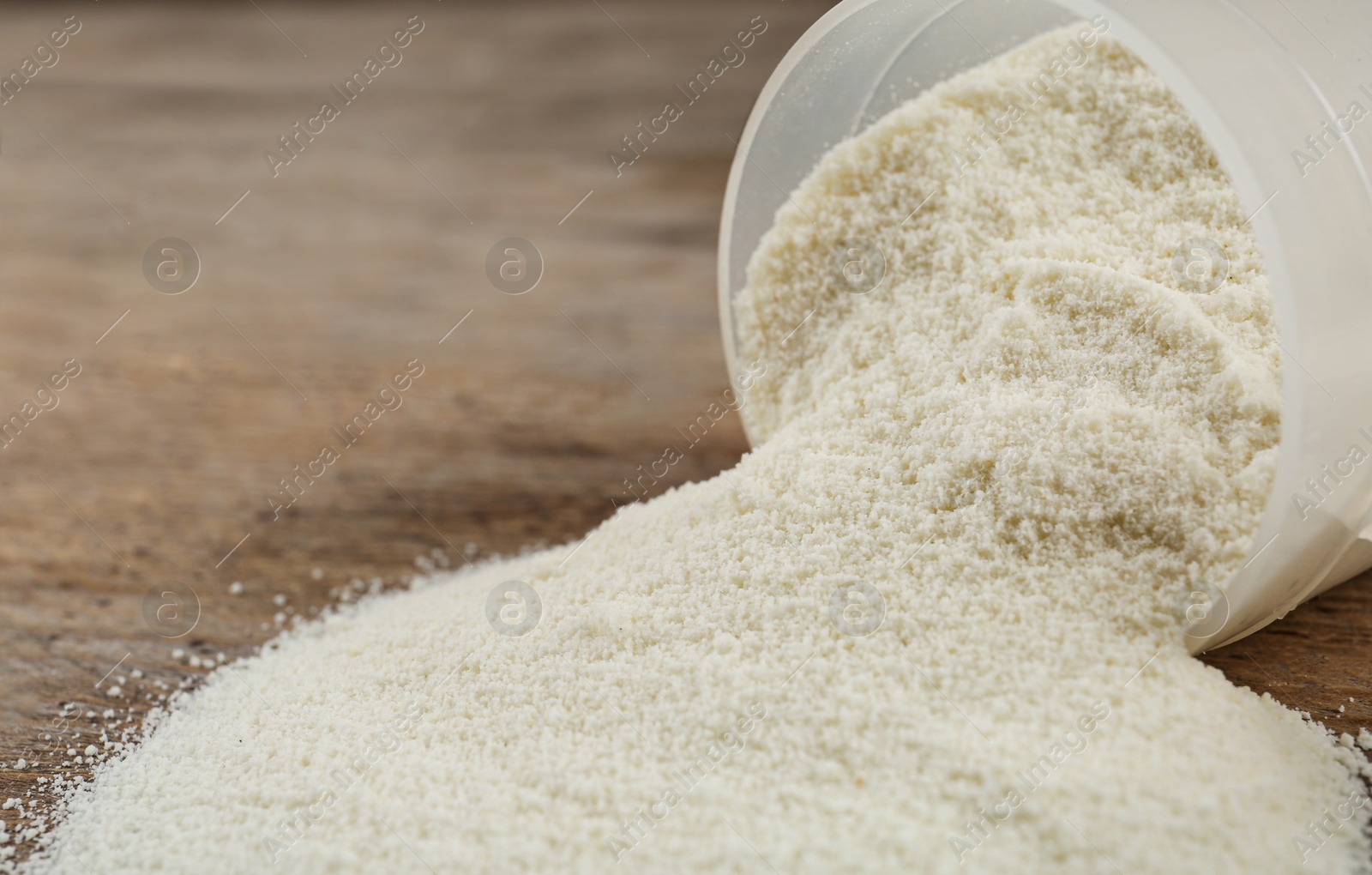 Photo of Overturned measuring scoop with protein powder on wooden table, closeup