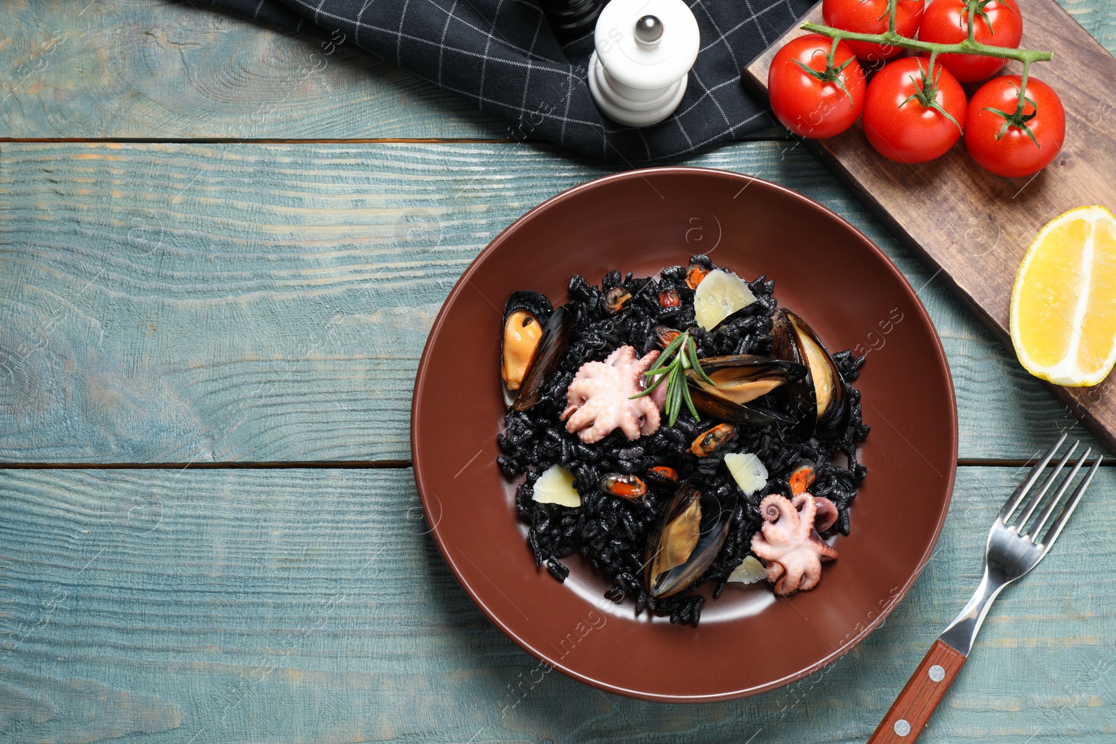 Photo of Delicious black risotto with seafood served on blue wooden table, flat lay