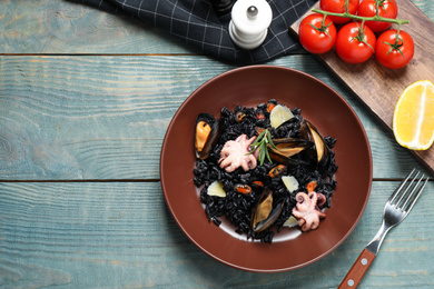 Photo of Delicious black risotto with seafood served on blue wooden table, flat lay