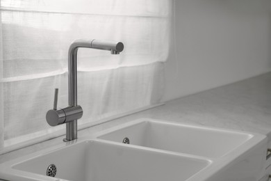 Photo of Modern sink and water tap near window in kitchen. Interior design
