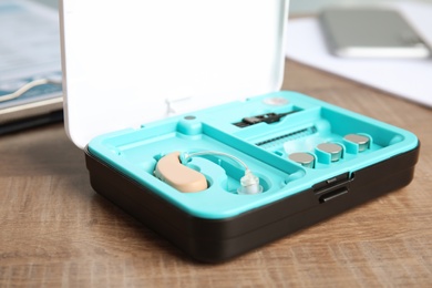 Photo of Box with hearing aid set on wooden table. Medical device