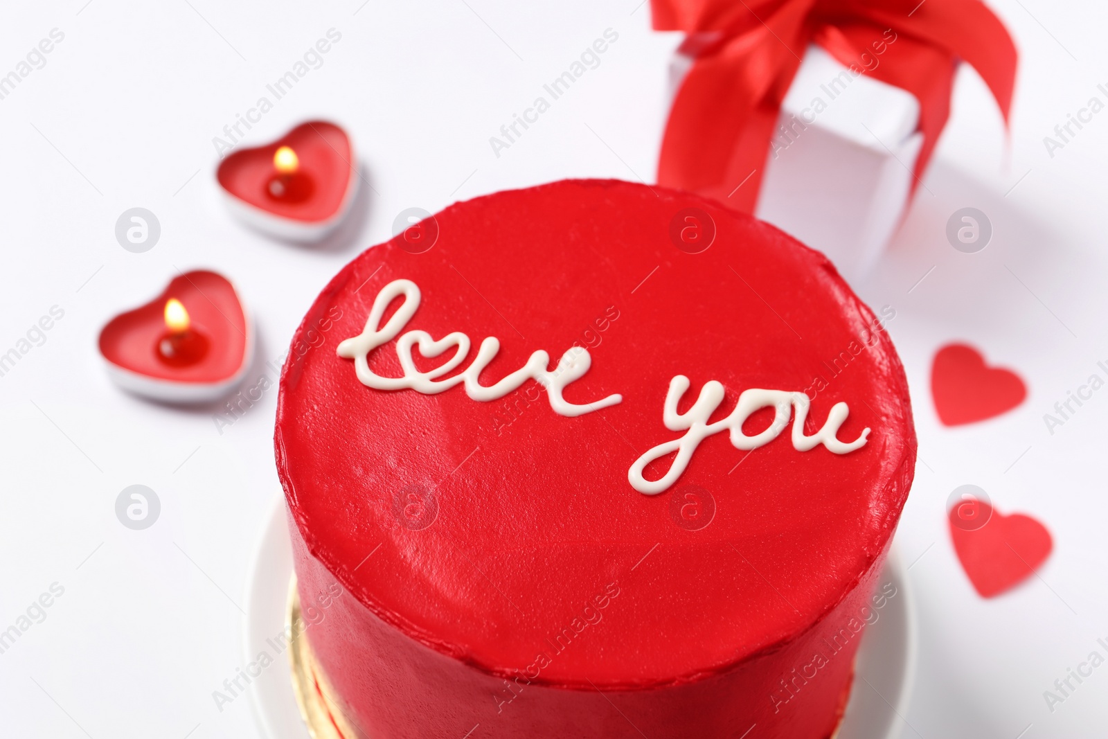 Photo of Bento cake with text Love You, candles, gift box and paper hearts on white table, closeup. St. Valentine's day surprise