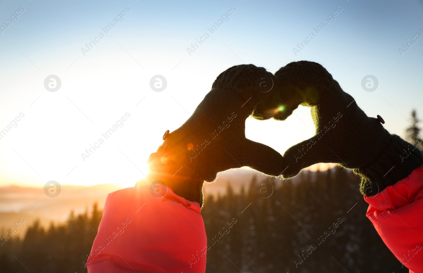 Photo of Woman making heart with hands outdoors at sunset, closeup. Winter vacation