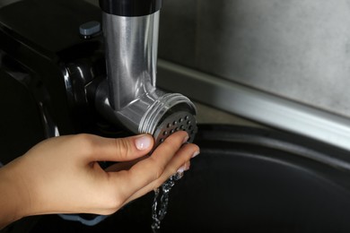 Woman washing electric meat grinder in kitchen sink indoors, closeup. Space for text