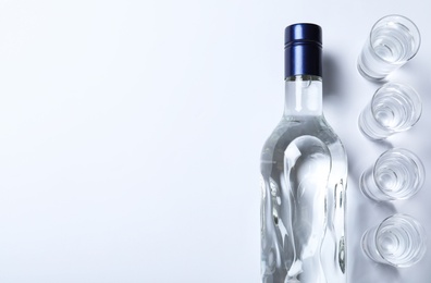 Bottle of vodka and shot glasses on white background, flat lay. Space for text