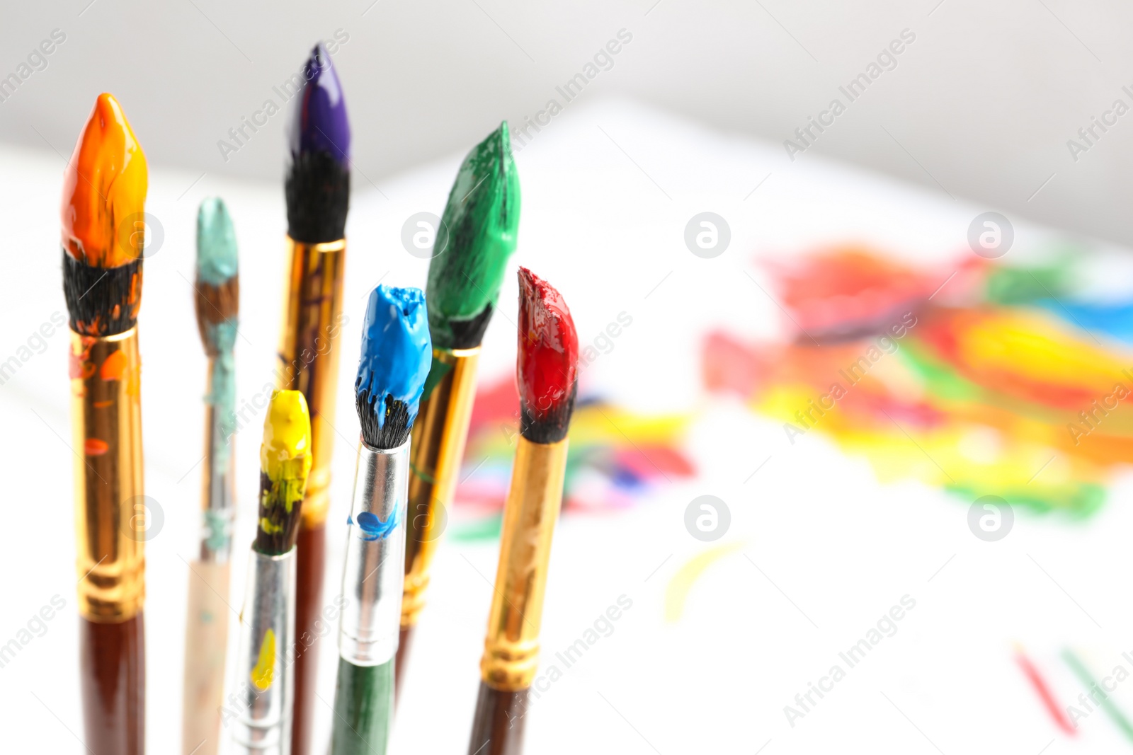 Photo of Brushes with colorful paints on blurred background, space for text