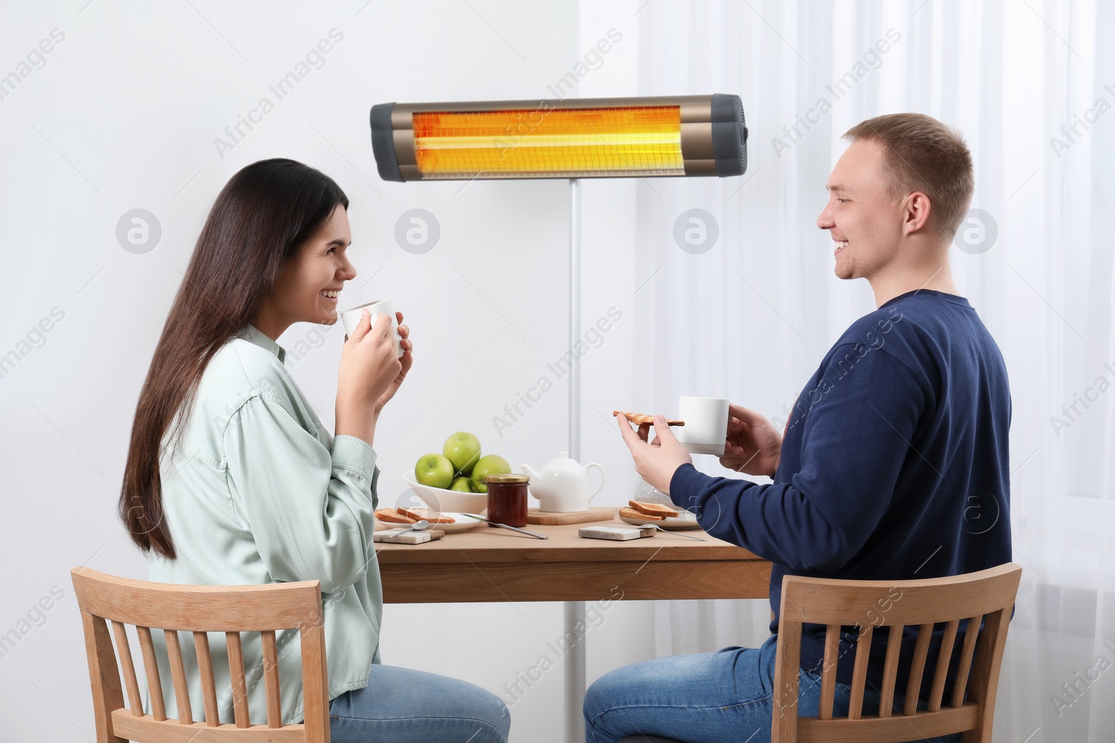 Photo of Couple spending time in room with modern electric infrared heater, focus on appliance