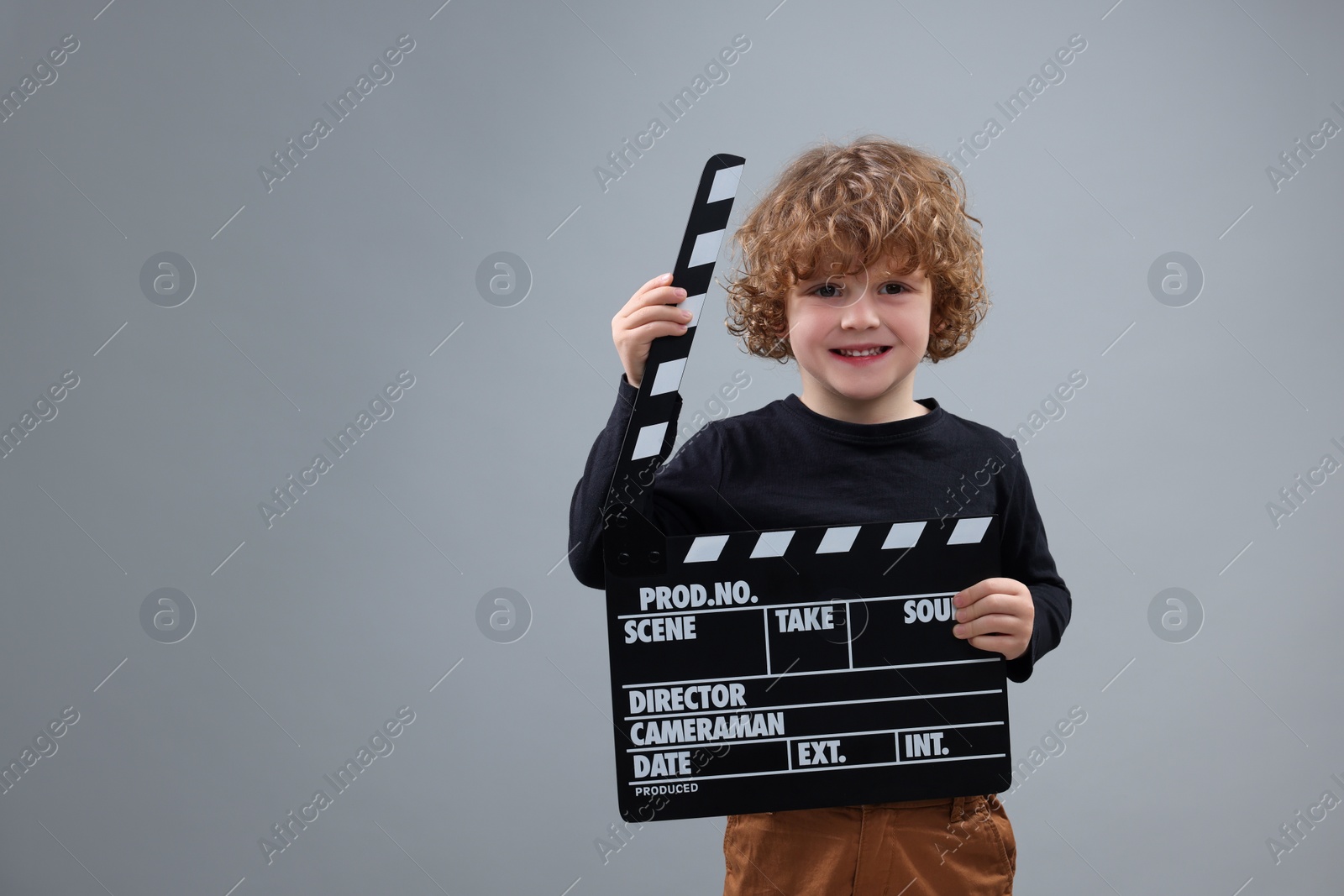 Photo of Smiling cute boy with clapperboard on grey background, space for text. Little actor