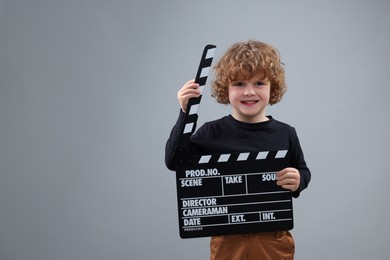 Photo of Smiling cute boy with clapperboard on grey background, space for text. Little actor