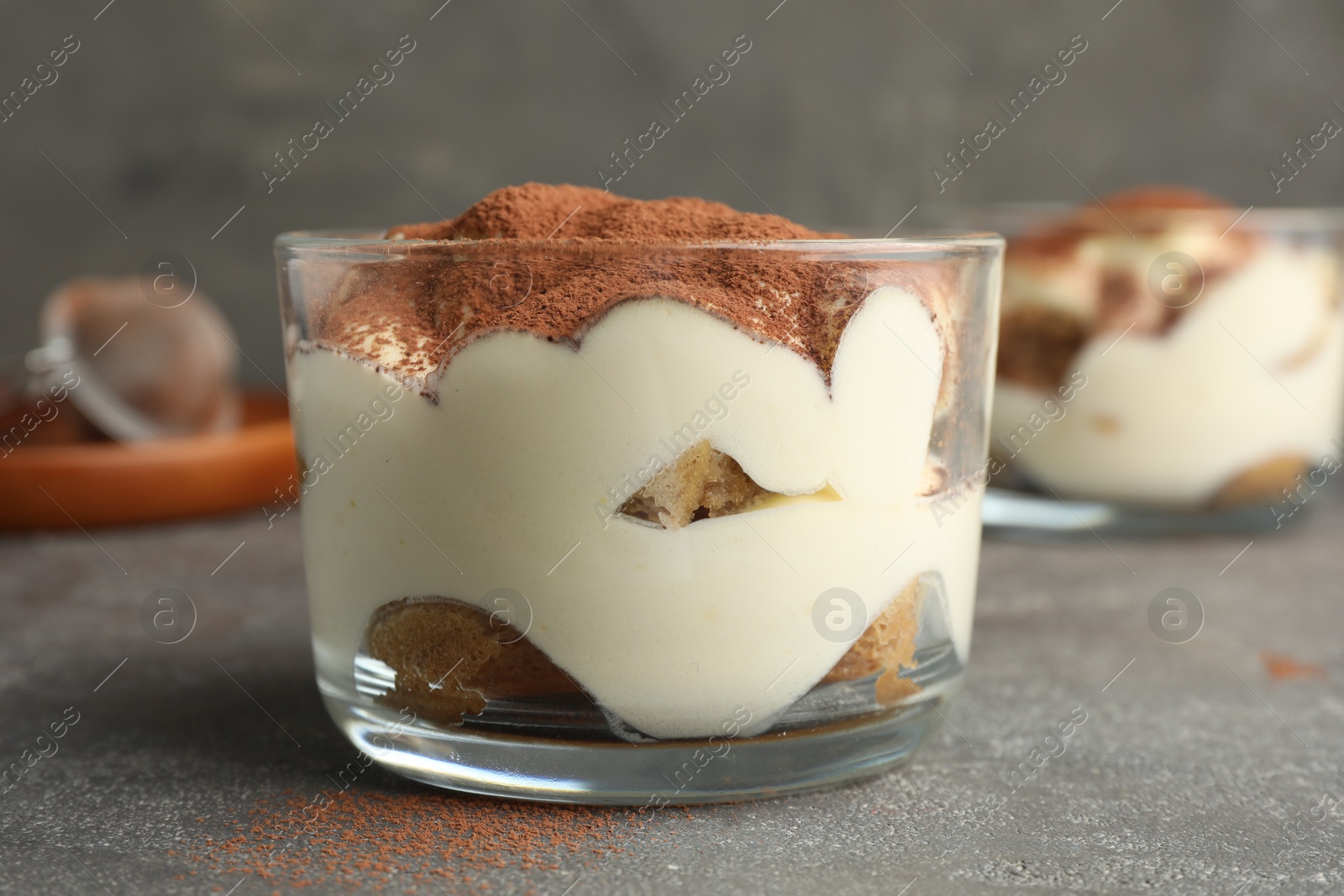 Photo of Delicious tiramisu in glass on grey table