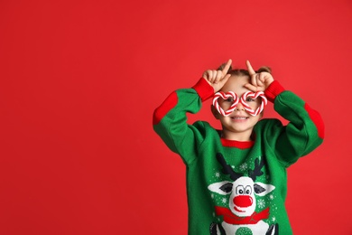 Cute little girl in Christmas sweater and party glasses on red background, space for text
