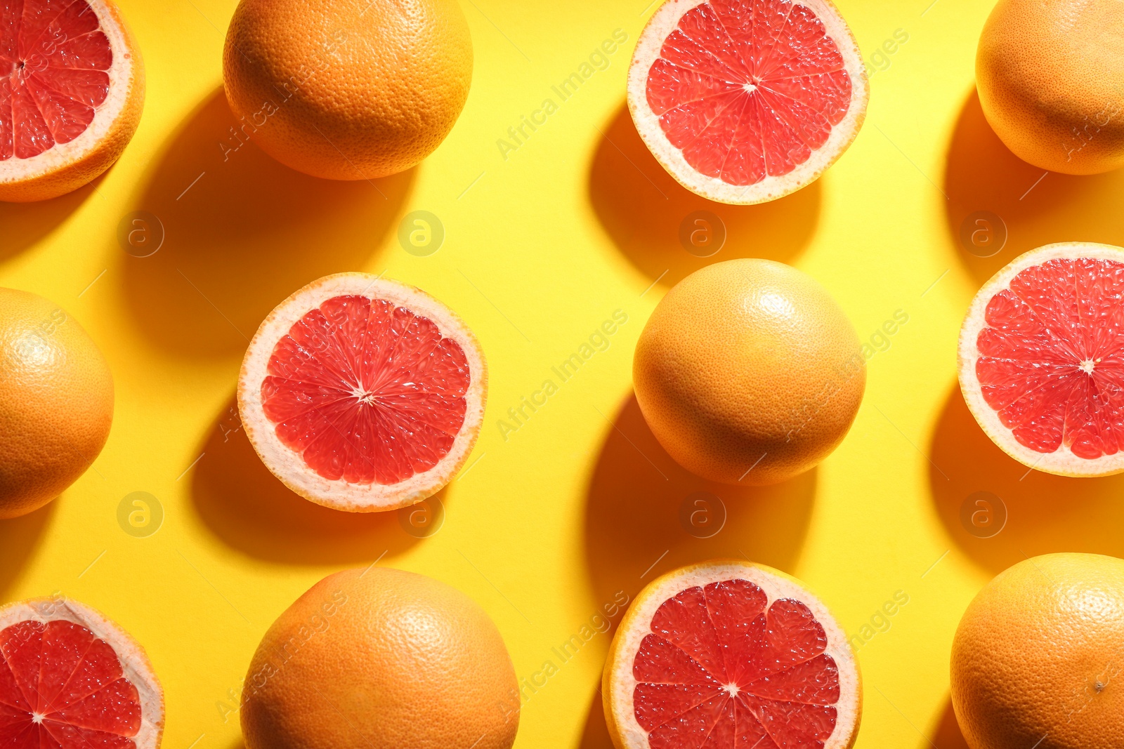 Photo of Cut and whole ripe grapefruits on yellow background, flat lay