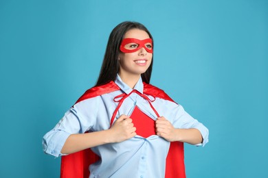 Confident young woman wearing superhero costume under shirt on light blue background