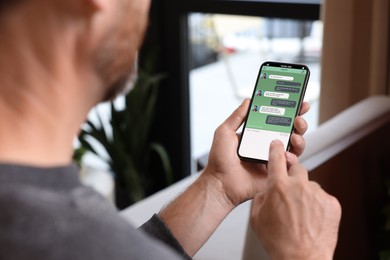 Image of Man texting via mobile phone indoors, closeup. Device screen with messages