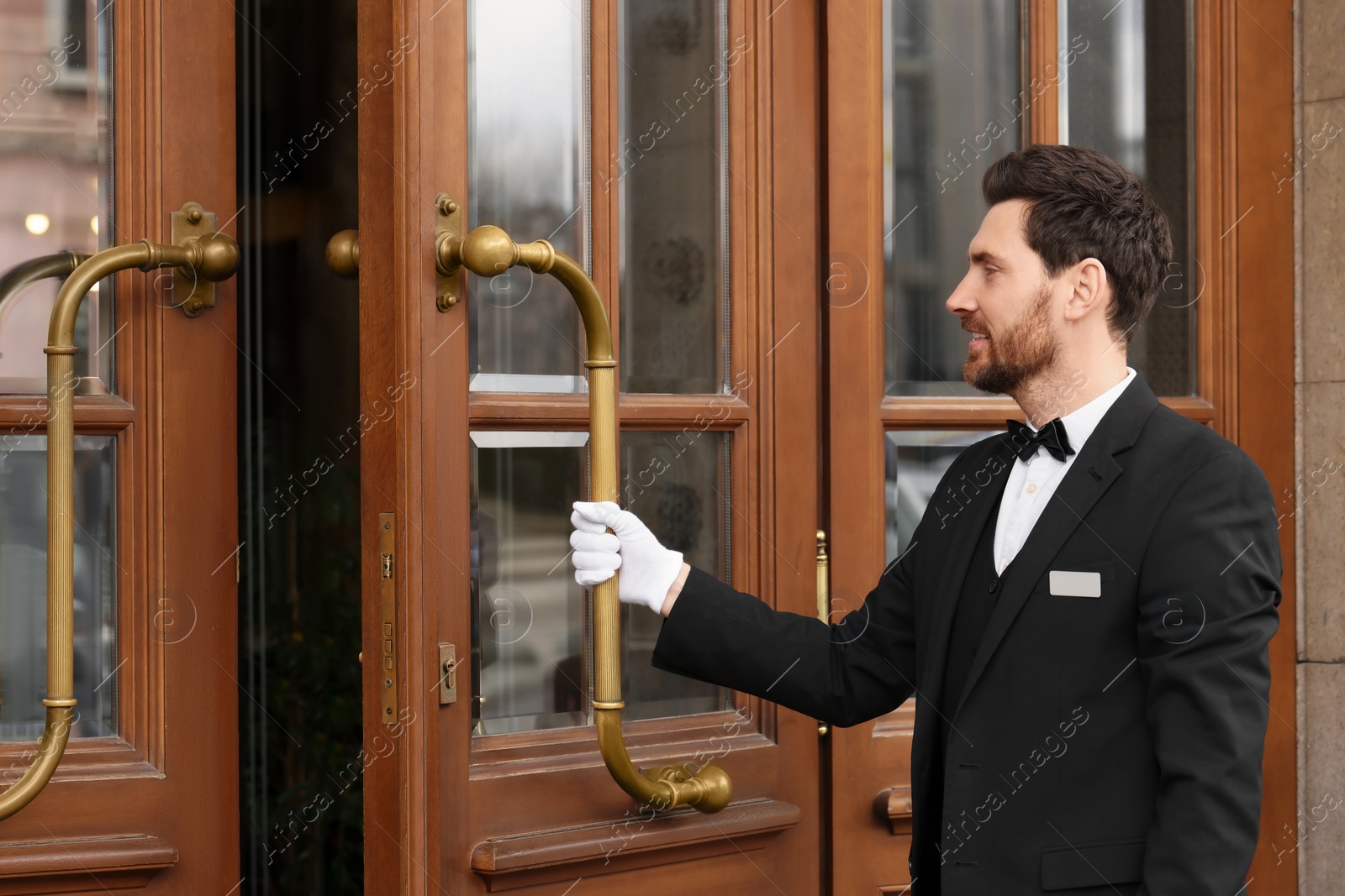 Photo of Butler in elegant suit and white gloves opening wooden hotel door. Space for text