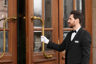 Butler in elegant suit and white gloves opening wooden hotel door. Space for text
