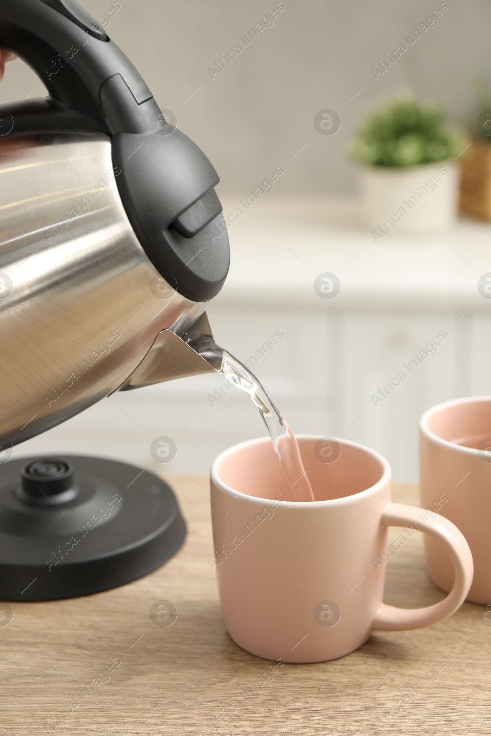 Photo of Woman pouring hot water from electric kettle into cup in kitchen, closeup