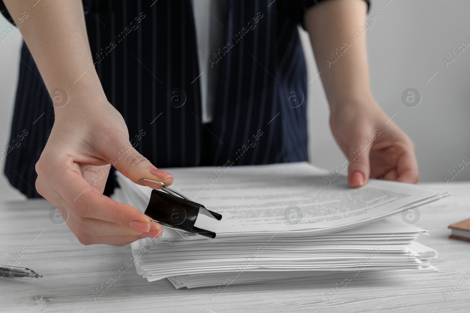 Photo of Woman attaching documents with metal binder clip at white wooden table in office, closeup