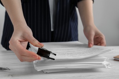 Woman attaching documents with metal binder clip at white wooden table in office, closeup