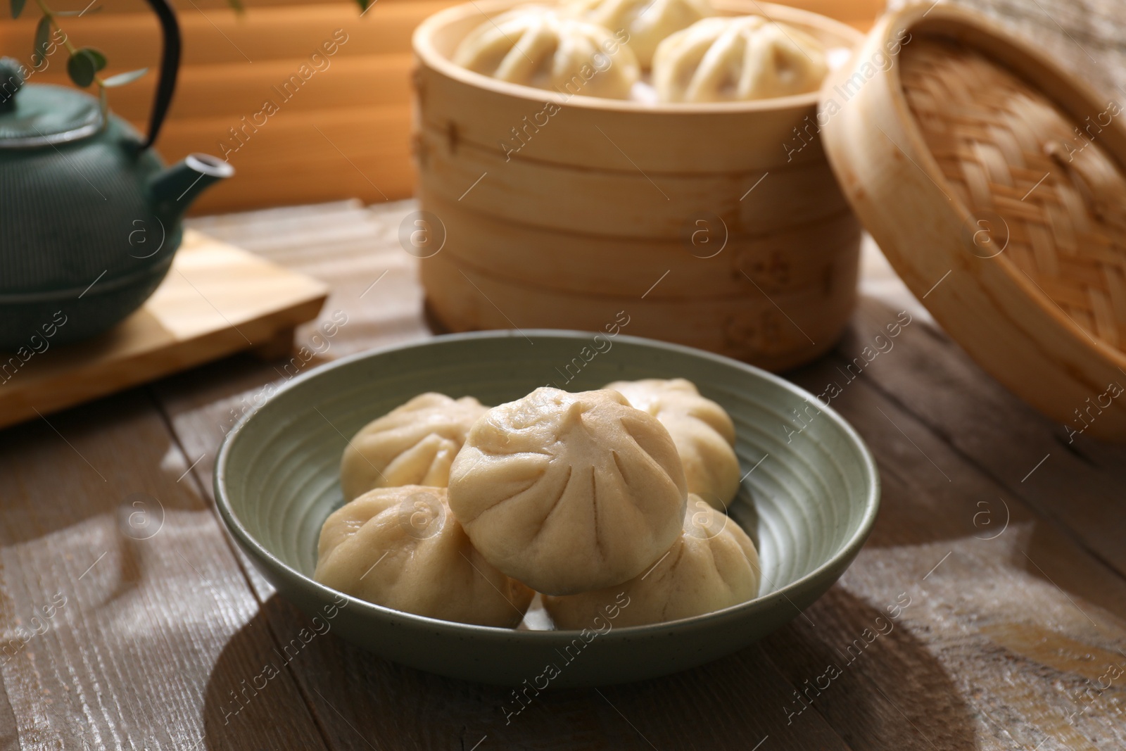 Photo of Delicious bao buns (baozi) in bowl on wooden table, closeup