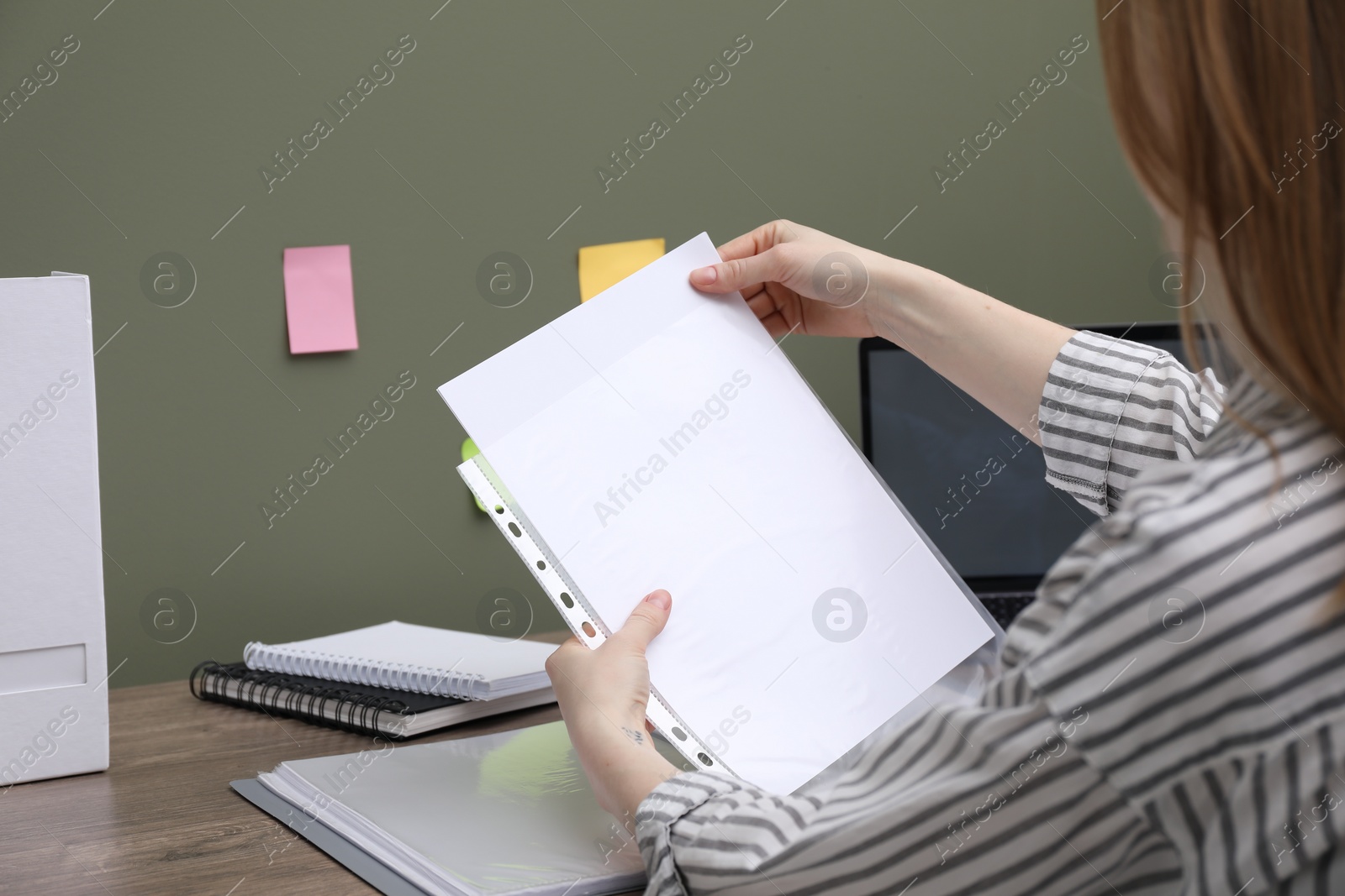 Photo of Woman putting paper sheet into punched pocket at wooden table, closeup