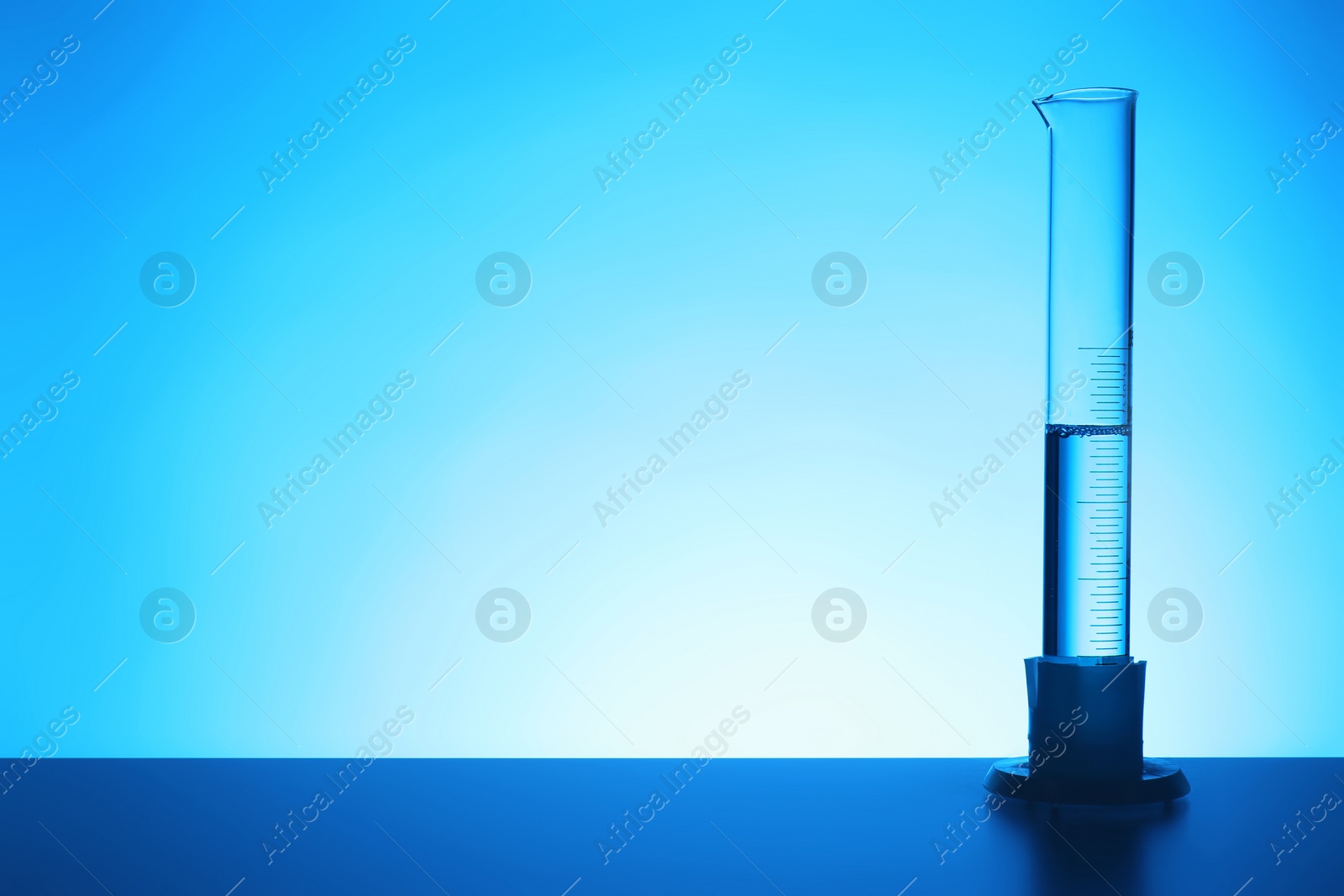 Photo of Graduated cylinder with liquid on table against color background. Chemistry laboratory glassware