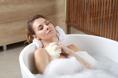 Photo of Beautiful woman with sponge taking bath indoors