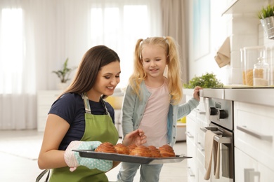 Photo of Daughter and mother with tray of oven baked buns in kitchen