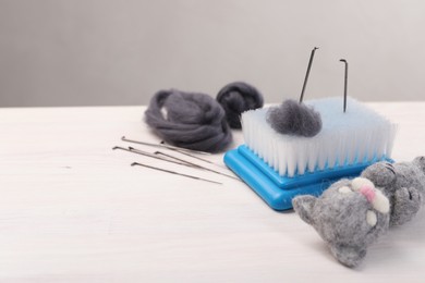 Photo of Felting tools, wool and toy cat on light wooden table. Space for text