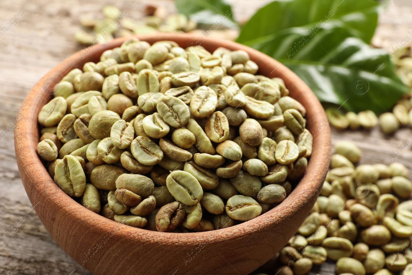 Photo of Green coffee beans and leaves on wooden table, closeup