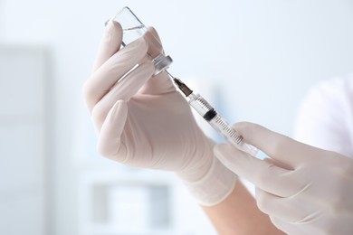 Doctor filling syringe with medication from vial on blurred background, closeup