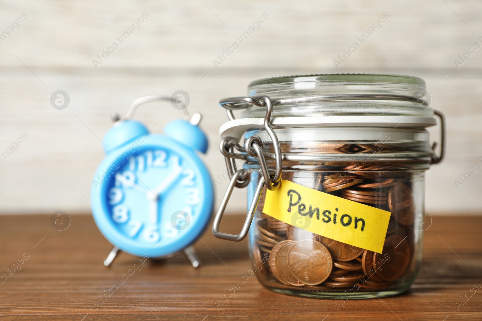 Photo of Coins in glass jar with label "PENSION" on table against light wall. Space for text