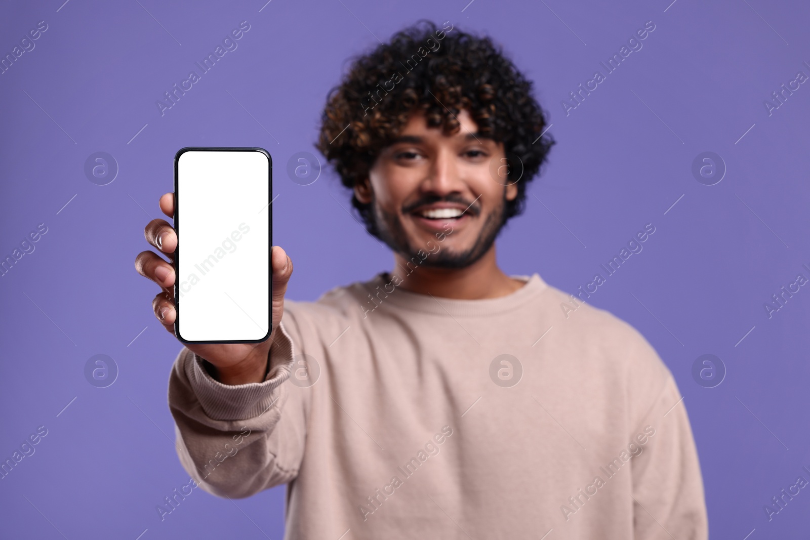 Photo of Handsome smiling man showing smartphone on violet background, selective focus