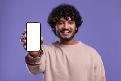 Handsome smiling man showing smartphone on violet background, selective focus