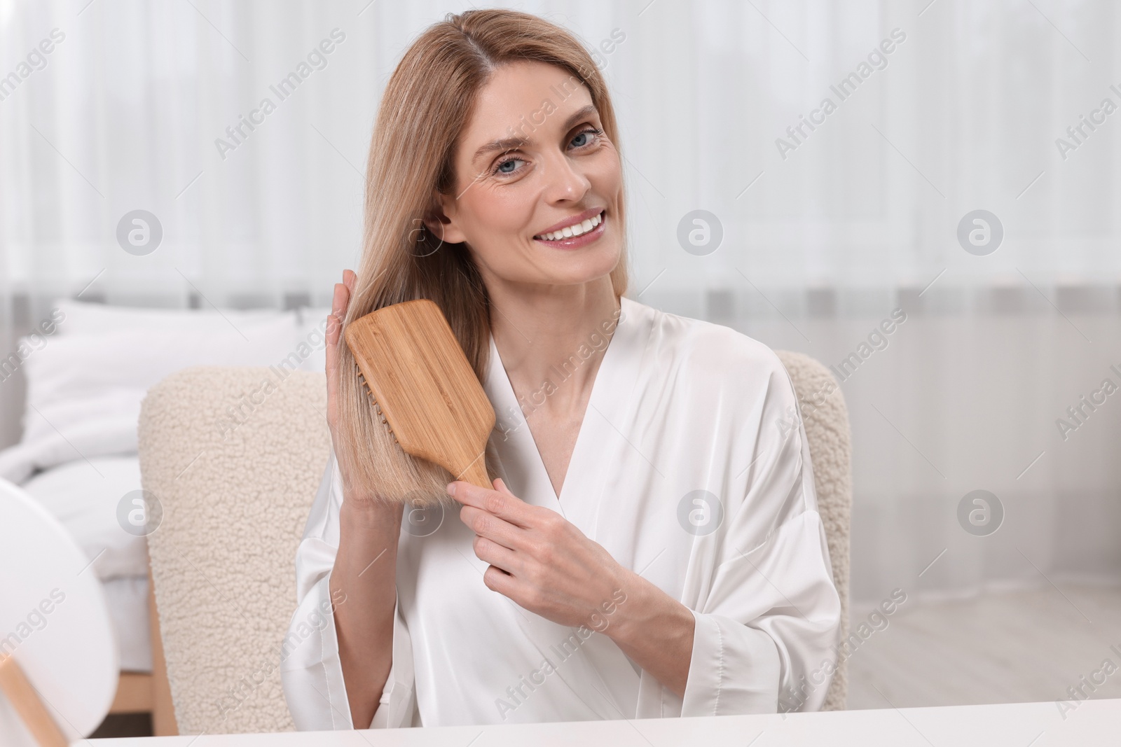 Photo of Beautiful happy woman brushing her hair in bedroom