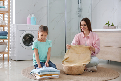 Photo of Mother and little daughter with clean laundry in bathroom