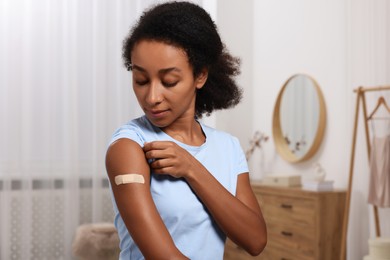 Young woman with adhesive bandage on her arm after vaccination indoors