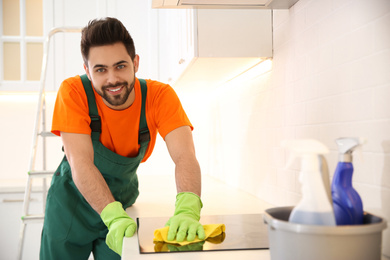 Photo of Professional young janitor cleaning stove in kitchen