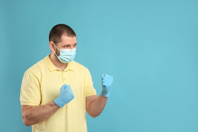 Photo of Man with protective mask and gloves in fighting pose on light blue background, space for text. Strong immunity concept