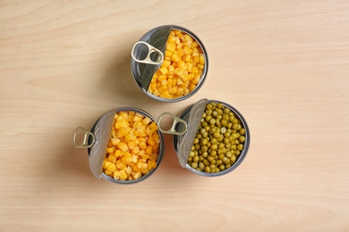 Open tin cans of conserved vegetables on wooden table, flat lay