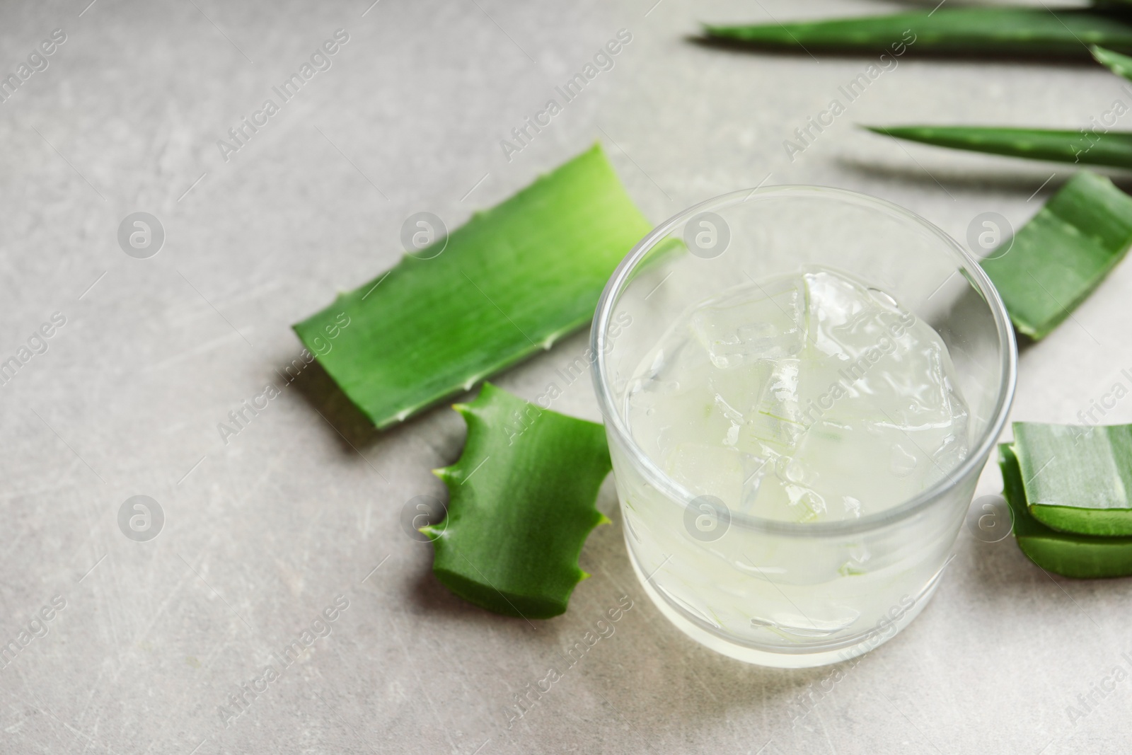 Photo of Glass with peeled aloe vera and green leaves on gray table