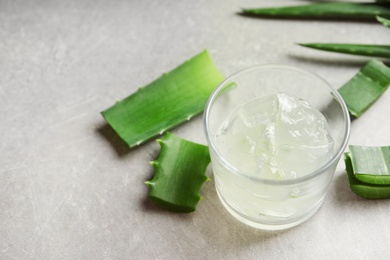 Glass with peeled aloe vera and green leaves on gray table