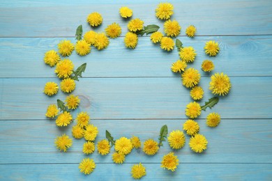 Frame of beautiful yellow dandelions on light blue wooden table, flat lay. Space for text