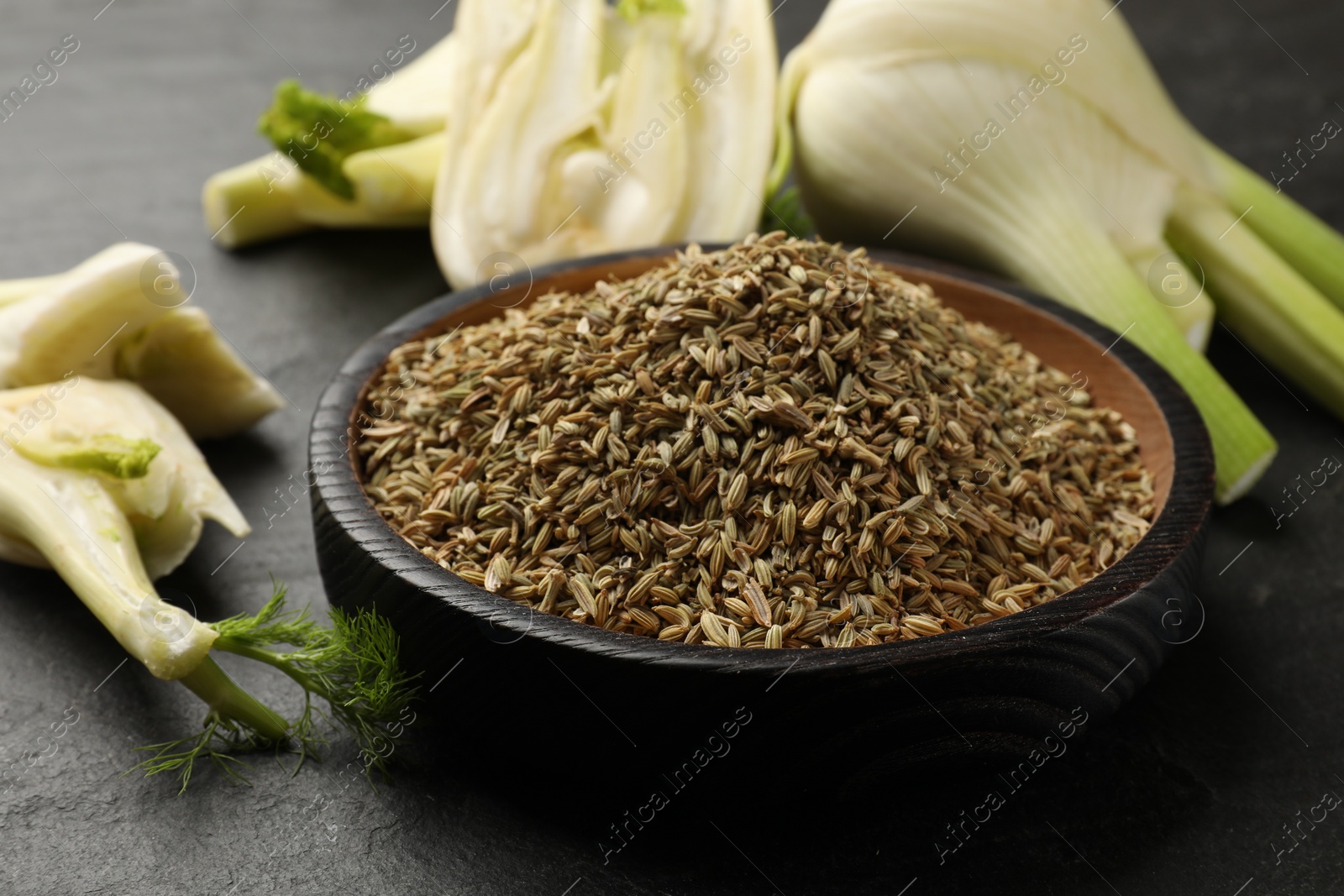 Photo of Fresh fennel bulbs and seeds in bowl on gray table, closeup