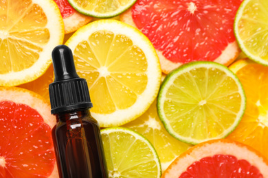 Bottle of essential oil on pile of citrus slices, flat lay. Space for text