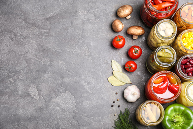 Photo of Glass jars with different pickled vegetables on grey table, flat lay. Space for text