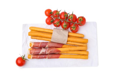 Photo of Delicious grissini sticks with prosciutto and tomatoes on white background, top view