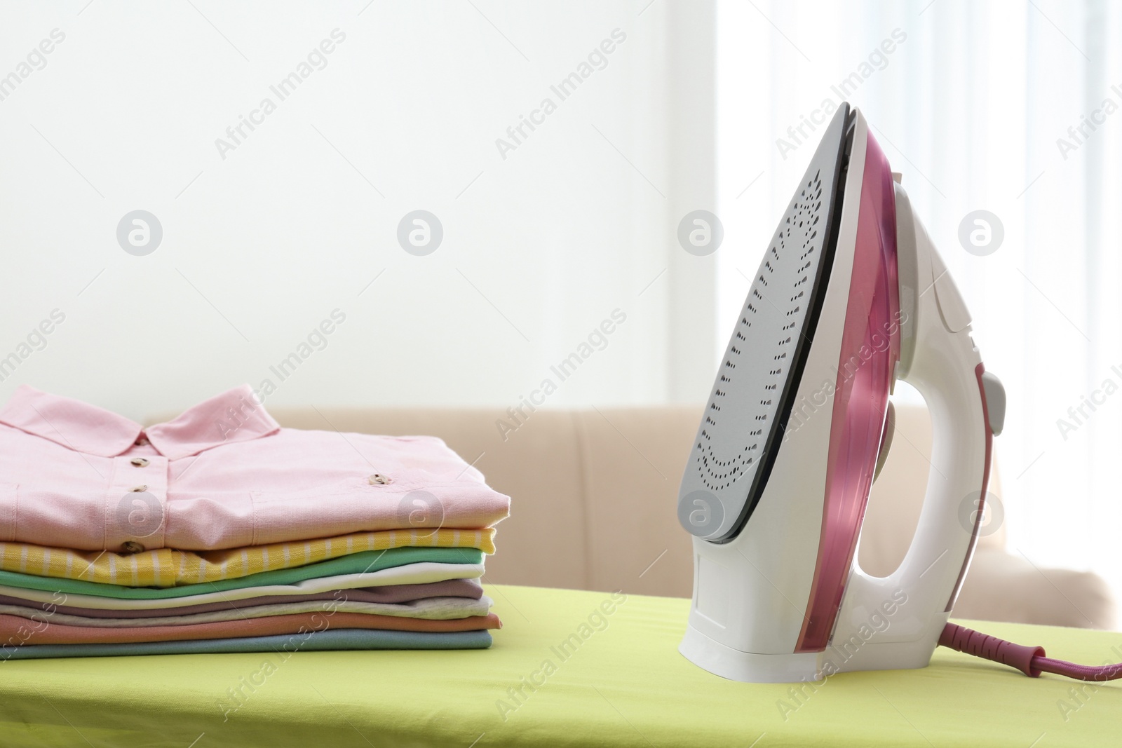 Photo of Board with modern iron and clean laundry at home