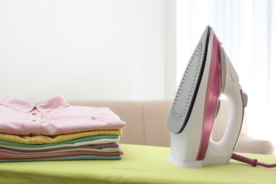 Photo of Board with modern iron and clean laundry at home